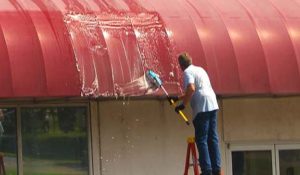 Mike Jackson standing on a ladder using a soft-bristled brush to clean a commercial awning.